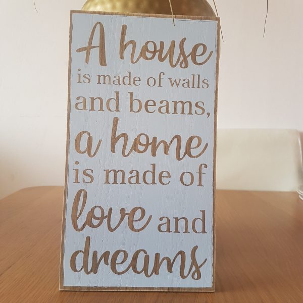 Wooden sign with the text 'A house is made of walls and beams, a home is made of love and dreams