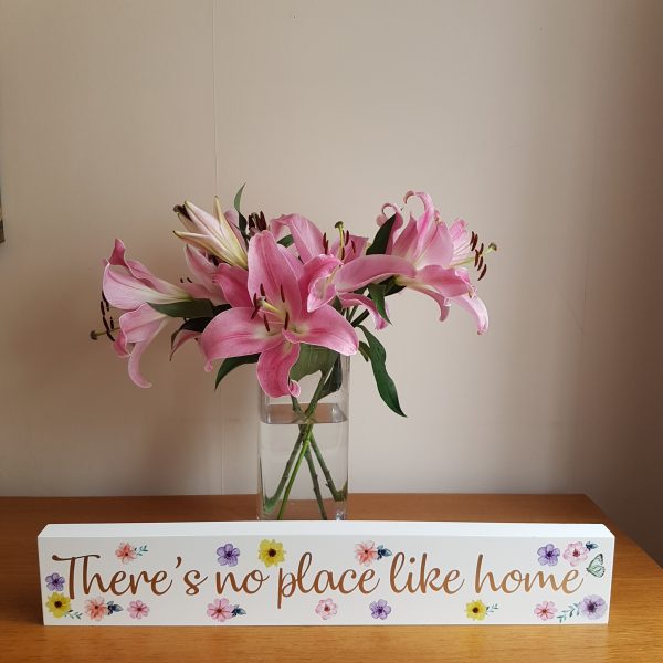 A large white free standing block with the text 'There's No Place Like Home' decorated with colourful flowers.