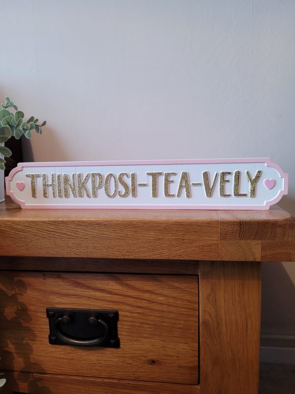 A white free standing block with a pink border with gold glitter text 'Think Posi-Tea-Vely'. With cute pink hearts either side, a fabulous sign for tea lovers!